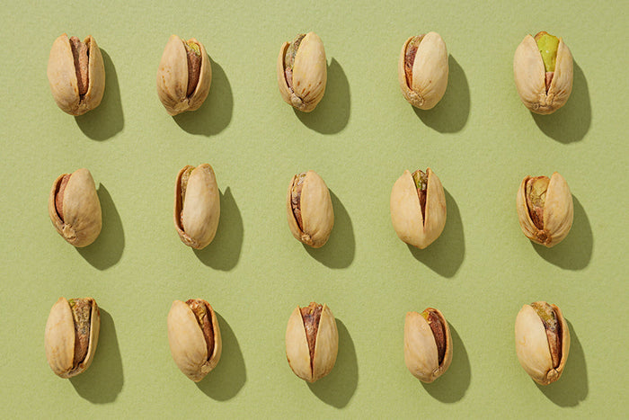 Aufgereihte Pistazien in der Schale auf grünem Hintergrund